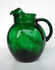 a green glass vase sitting on top of a white table next to a black handle