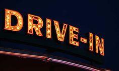 a drive - in sign lit up at night with the word drive - in below it