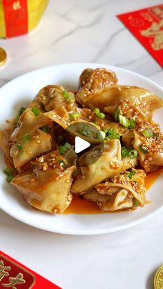 a white plate topped with dumplings covered in sauce and green onions on top of a table