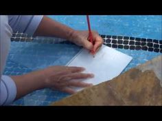 a person writing on a piece of paper next to a swimming pool with blue tiles