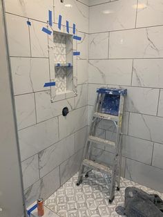 a ladder is in the corner of a bathroom with white tiles and blue tape on the walls