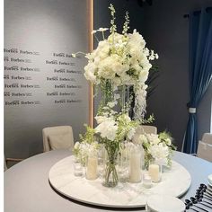 white flowers and candles are arranged on a round table in front of a wall with writing