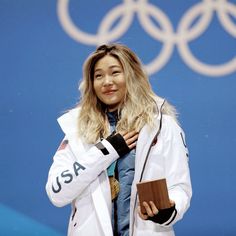 a woman holding a gold medal in front of a blue wall with the olympic rings behind her