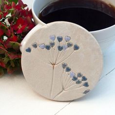 a ceramic coaster with blue hearts on it next to a cup of coffee and flowers