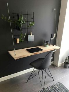 a desk with two chairs and a laptop on it in front of a gray wall