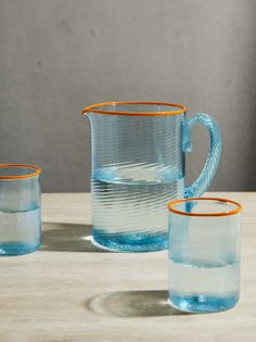 three blue glass pitchers and two orange rimmed glasses sitting on a wooden table top