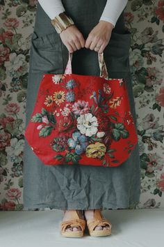 a woman is holding a red bag with flowers on it