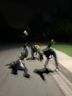 a group of young men riding skateboards down a street at night with their hands in the air