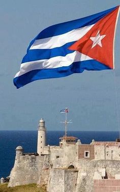 a large flag flying in the wind next to an old brick wall and lighthouse tower