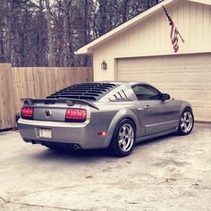 a gray sports car parked in front of a house with an american flag on it