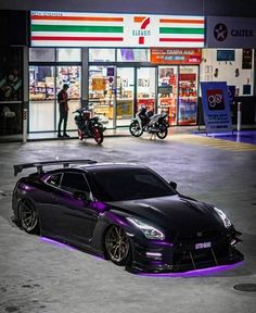 a black sports car parked in front of a gas station with purple lights on it