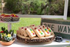 desserts and cupcakes are displayed on an outdoor table in front of a one way sign