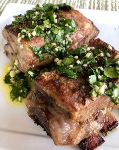 two pieces of meat sitting on top of a white plate covered in green garnish