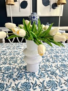 a white vase filled with flowers on top of a blue and white tablecloth covered table