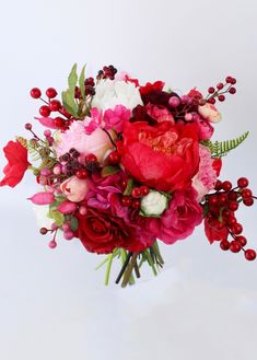 a bouquet of red and pink flowers on a white background with berries in the center