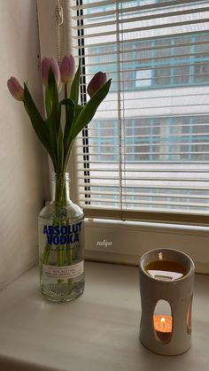 a vase filled with flowers next to a lit candle on a window sill in front of a window