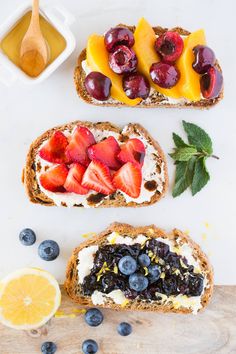 three slices of bread with fruit on top and blueberries, oranges, and strawberries