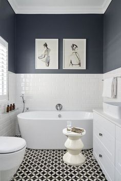 a white bath tub sitting next to a toilet under two pictures on the wall in a bathroom