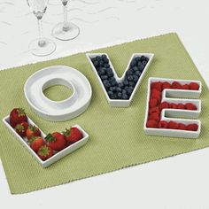 the word love spelled out with fruits and berries in front of two wine glasses on a table