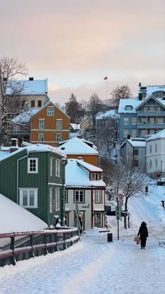 a person walking down a snow covered street with buildings in the backgrouds