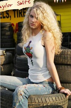 a woman sitting on top of a pile of tires wearing jeans and a tank top