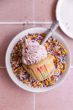 a cupcake with pink frosting and sprinkles in a white bowl