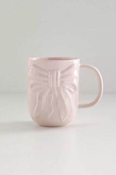 a pink coffee cup with a butterfly design on the front and sides, sitting on a white surface