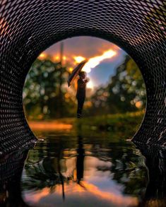 a person holding an umbrella standing in the middle of a body of water at sunset