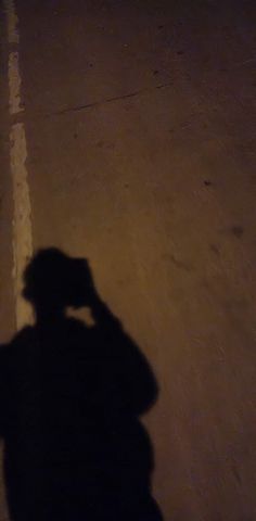 the shadow of a person standing in front of a parking lot holding a cell phone to their ear