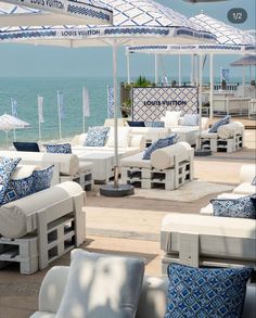 an outdoor seating area with blue and white cushions, umbrellas and water in the background