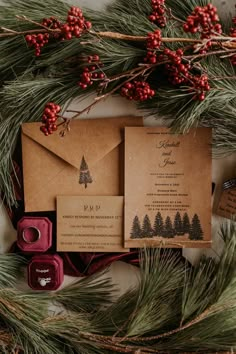 the wedding stationery is surrounded by pine branches and red wax stampers, which are also decorated with berries