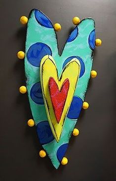 a heart shaped decoration hanging from the side of a black wall with yellow and blue balls around it