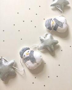 snowman and penguin ornaments hanging from string on white surface with stars in the background