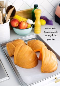 two peeled apples sitting on top of a baking pan next to a bowl of fruit