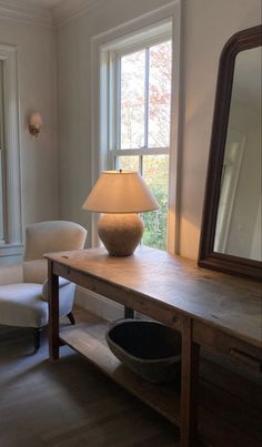 a lamp sitting on top of a wooden table next to a mirror and chair in a room