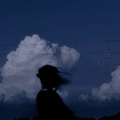 the silhouette of a person standing in front of a cloud with birds flying over it