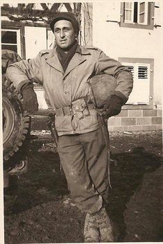 an old photo of a man in uniform standing next to a tractor and holding his hands on his hips