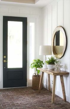 a room with a door, mirror and potted plants on the table in front of it