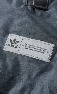 an adidas label on the back of a grey jacket with white stitching and black trim