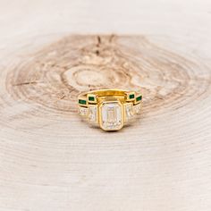 an emerald and diamond ring sitting on top of a piece of wood