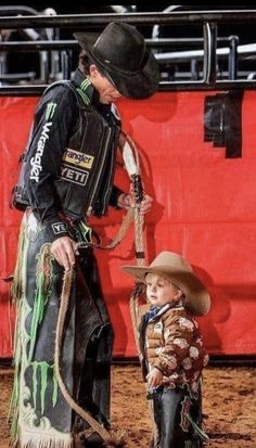 a man in cowboy attire standing next to a little boy wearing a hat and lasso