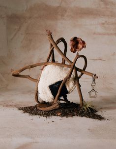 a sculpture made out of sticks and branches with a flower in the center, sitting on top of dirt