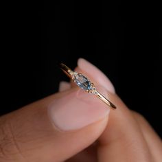 a woman's hand holding a ring with an oval shaped diamond on it and two small diamonds in the middle