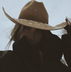 a woman wearing a cowboy hat with snow on the brim and her hair blowing in the wind