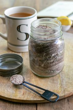 a wooden cutting board topped with a glass jar filled with dirt next to a measuring spoon