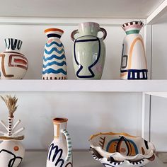 several vases and bowls are on shelves in a room with white walls behind them