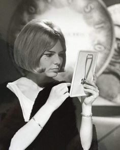 a black and white photo of a woman holding an item in her hand while looking at it