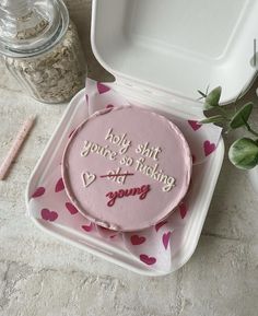 a pink cake sitting on top of a table next to a container with writing on it