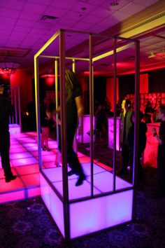 people standing around in a room with neon lights on the floor and one person walking