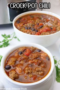 Two white bowls full of chili with the crock pot in the background.